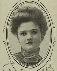 A portrait of a young white woman in an oval frame; she is wearing a high-collared blouse or dress, and her hair is in a bouffant updo. Her eyes appear to have been outlined with ink.