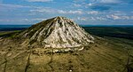 A white conical hill in a flat landscape, partially covered by forest