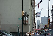 A bronze sign on the eastern end of the 14th Street facade. This sign is triangular and contains a pair of clock faces.