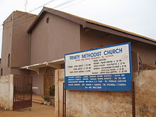 A brown church with a gate and a sign reading "Trinity Methodist Church".