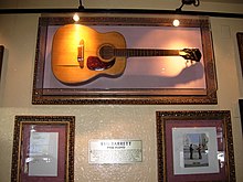 Guitare accrochée à un mur au-dessus de deux cadres.