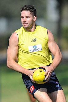 A man with short brown hair in a sleeveless yellow guernsey and black shorts