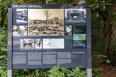 Panneau explicatif pour les visiteurs (2019) qui présentent diverses photos. Dans le sens des aiguilles d'une montre : 1. Vue de 1934, depuis le Wuckersee (de), montrant la Carinhall initiale ; 2. Photo de 1940 avec les travaux en cours pour la seconde extension ; 3. Un passant devant les ruines en 1947 ; 4. Portrait de Göring (1932) en uniforme SA ; 5. Plan de la bande de terre entre les deux lacs, avec la mention des deux extensions de Carinhall (1937 et 1940), Göring avait planifié la fin de la troisième extension (concernant un nouveau musée) pour 1953 ; 6. Plan du projet de cette troisième extension tel que présenté le 12 janvier 1945 ; 7. Visite du général japonais Oshima en mars 1940 ; 8. Göring reçoit le ministre des Affaires étrangères britannique, Lord Halifax, le 20 novembre 1937 ; 9. Le 19 juin 1934, Göring, accompagné de Hitler, sort de la crypte aménagée pour sa défunte épouse Carin, sur la rive nord du Wuckersee (de).