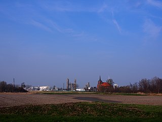 Het kerkje met de industrie op de achtergrond. Op de voorgrond het westelijke restant van de dorpswierde van Heveskes.