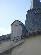 Photographie en couleurs d'une lucarne percée d'une porte en bois dans un toit.