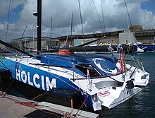 Voilier vert, bleu et blanc vu de trois quarts arrière, amarré au ponton.