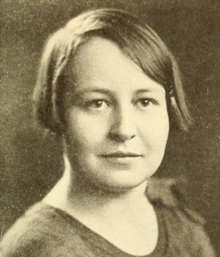 A young white woman with straight hair cut in a side-parted bob, wearing a barrette and a top with a scoop neckline