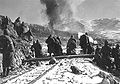 Soldiers watch a hill in front of them as aircraft drop bombs on it