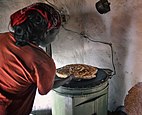 Une femme de dos cuisant du pain sur un meuble cylindrique vert et noir.