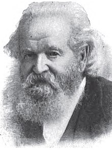 A man with long gray hair, a mustache, and a long gray beard wearing a black jacket and white shirt