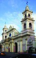 Frontis, Campanarios, Atrio y Galería lateral de la Catedral Basílica de Salta.Situada frente a la Plaza 9 de Julio, en el corazón del centro histórico de la Ciudad, esta Catedral integra un conjunto monumental con el Palacio Episcopal. Circunscribiéndonos a su parte más importante, en el año 1.873 con el fin de reanudar trabajos de construcción largamente paralizados, se contrató la construcción de la parte remanente y aún inconclusa, con la Empresa de los arquitectos Nicolás y Agustín Cánepa, excluyendo: frente, atrio, torres y galería al costado izquierdo desde la entrada a la sacristía. A partir de allí, pseudo investigaciones históricas, en algunos casos empeñados en deformar la verdad histórica sobre la autenticidad en la autoría del proyecto del frente, atrio y campanario, pretendieron y aun pretenden en esta ambigüedad, adjudicar su autoría a: ¿Bertrés?, ¿Soldati ?, ¿Georgi?, ¿Riguetti?, generando al día de la fecha, conclusiones erróneas fácilmente evitables. Un documento redescubierto por la Academia Nacional de Bellas Artes, merced a la búsqueda de documentación efectuada por la investigadora de campo, Sra. Iris Gori, bajo la supervisión del académico de número Prof. Héctor H. Schenone, restablece merced a este hallazgo de modo fehaciente, que el verdadero autor del diseño es el Sr. Maqui (apellido escrito alternativamente como Maqui o Macchi por el propio arquitecto Macchi, a fin de facilitar su pronunciación). A fs.271,el libro Patrimonio Artístico Nacional, Academia Nacional de Bellas Artes, Bs. As. año 1988, dejó consignado: «...Hemos podido levantar una interesante noticia en el Diario salteño «La Reforma» del 28 de junio de 1879 (pág. 2, 3era. columna): «...Por 29000 $ se ha contratado la obra del frontis de la Catedral, con el empresario Riguetti según el plano del Señor Maqui...».