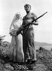 Black and white photo of Robert Mitchum holding a gun standing next to Deborah Kerr in the movie Heaven Knows Mr. Allison in 1957