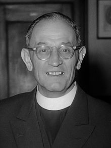 Black and white photograph of Martin Niemöller. He is a white middle-aged man wearing clerical clothing and glasses.