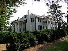 Large, classic style white house surrounded by lots of greenery.