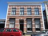 Groot woonhuis, in rij van drie op elkaar gelijkende panden. In straatwand gelegen, met rechts smalle poortdoorgang en links zijgevel met aanbouw.