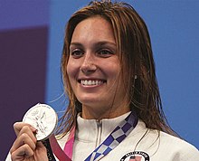 Walsh im weißen Trainingsanzug mit dem Wappen der Vereinigten Staaten. Mit der rechten Hand präsentiert sie ihre Medaille.