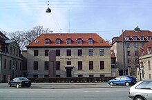 A block-shaped beige building with a sloped, red tiled roof