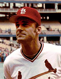 A man in a white baseball uniform and red cap.