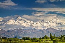 Des montagnes aux sommets dans les nuages mais avec des pentes enneigées avec une belle luminosité.