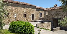 Photo of a building of rough stone with small windows, surrounded by olive trees