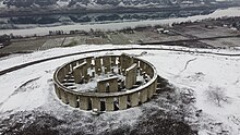 Wide aerial view of the Stonehenge, looking south across the Columbia to Oregon. Snow dusts the monument and surrounding countryside.