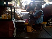 Woman preparing tlacoyos over the sidewalk in Colonia Condesa in Mexico City. The tlacoyo is cooked over a comal which is over an anafre, a kind of coal stove used in Mexican households without any heating energy