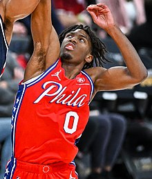 Maxey, in a red basketball jersey with the number 0, is jumping and reaching for a basketball.