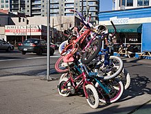 Photograph of a pile of small bicycles, intertwined at a street corner