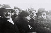 A black-and-white photo of two men in hats with a woman between them.