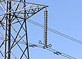 Detail of the insulators (the vertical string of discs) and conductor vibration dampers (the weights attached directly to the conductors) on a 275,000 volt suspension tower near Thornbury, South Gloucestershire, England, United Kingdom