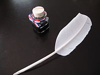 Picture of a quill and a small bottle of ink on a table.