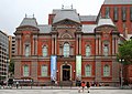 Photograph of the Renwick Gallery, an old brick building with colorful contemporary banners flanking the main entry and announcing "American Craft".