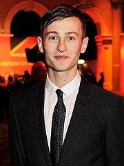 A dark-haired man wearing suit and tie poses for the camera