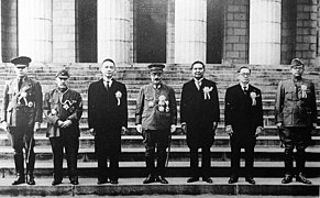 Photo de sept hommes en uniformes, en extérieur, sur les marches d'un bâtiment. Ils sont alignés de face.