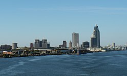 A large city seen from the water on a clear day. The shoreline is fringed with docks above which rise city buildings including several skyscrapers.