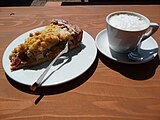 Piece of rhubarb cake with crumbles, next to a cup of cappuccino