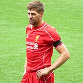 The head and torso of a man with short, brown hair. He is wearing a red shirt and a black armband.