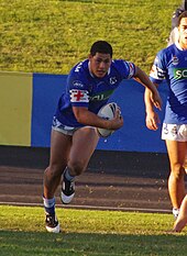 Photographie d'un homme portant un maillot de rugby bleu, tenant un ballon de rugby.