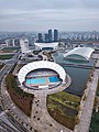 Das SOSC mit dem Schwimmstadion im Vordergrund. Rechts dahinter liegt die Schwimmhalle. Im Hintergrund das Hallenstadion. Links daneben steht das Medienzentrum. (März 2018)