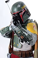 Homme dans une armure futuristique verte jaune et rouge usée, pointant un pistolet laser vers le photographe.