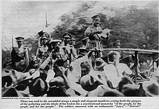 People gathering around a man standing on a possibly podium reading a declaration, all of them wearing soldier or related uniforms