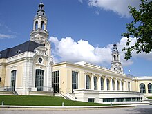 Photographie en couleurs d'un long bâtiment terminé par deux pavillons couverts de clochetons.