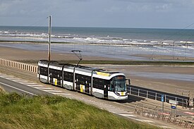 Five-section tram running on track between a road and a beach