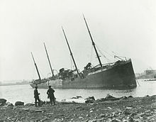 Two men observe a large, beached ship with "Belgian Relief" painted on her side