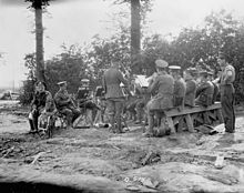 Photographie en noir et blanc d'une fanfare militaire en train de jouer avec les musiciens assis et le chef d'orchestre debout devant eux