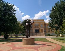 A statue of a woman in Native American costume in front of a yellow brick three-story building.