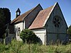 A stone church seen from the south east with steep tiled roofs. Nearest is the chancel with a round east window, beyond that is a larger, higher nave, at the end of which is a bellcote