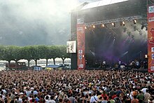 Photographie en couleurs d'une scène et du public d'un concert en plein air.