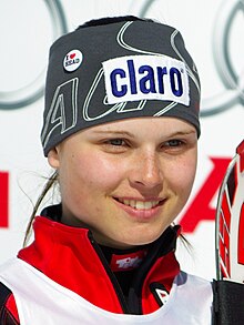 Portrait d’une jeune femme, souriante, vêtu d’une veste de ski rouge et d’un bandeau gris, avec une publicité