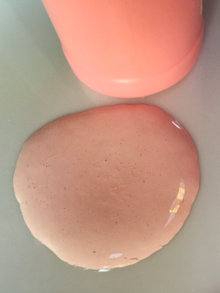 A puddle of a thin pink lotion, next to a pink plastic bottle